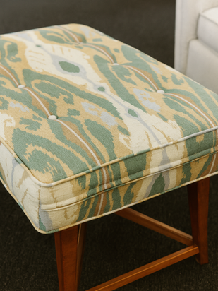 A tufted rectangular ottoman cushion with green, beige, and white ikat pattern.