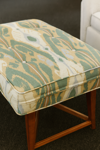 A tufted rectangular ottoman cushion with green, beige, and white ikat pattern.
