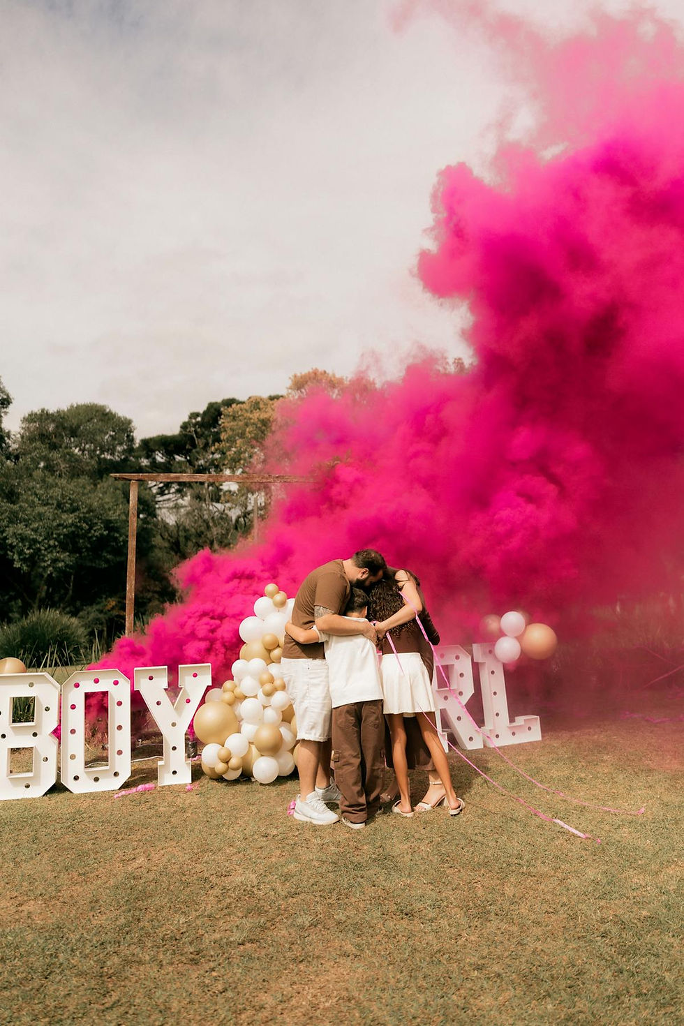 Family celebrating a gender reveal with pink smoke outdoors