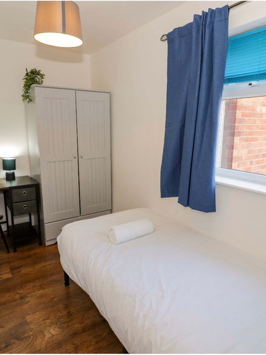 Small bedroom with single bed, desk, wardrobe, and blue curtains.