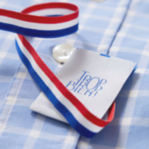 Image d’une chemise élégante sur fond bleu et blanc, mettant en avant son étiquette en carton éco-responsable. L’étiquette affiche le message Trop Trop Bien ! avec un design moderne et épuré. Un ruban bleu, blanc, rouge traverse l’étiquette au milieu, symbolisant fièrement la fabrication française et le savoir-faire local. Cette mise en scène reflète à la fois l’engagement écologique et la qualité artisanale du produit.
