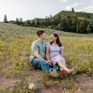 Couple sitting together in the mountains holding hands and looking at each other lovingly.