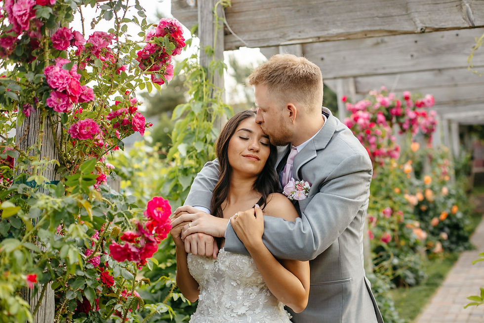 Documentary-style wedding photography cover photo. Bride and groom snuggling by pink flowers.