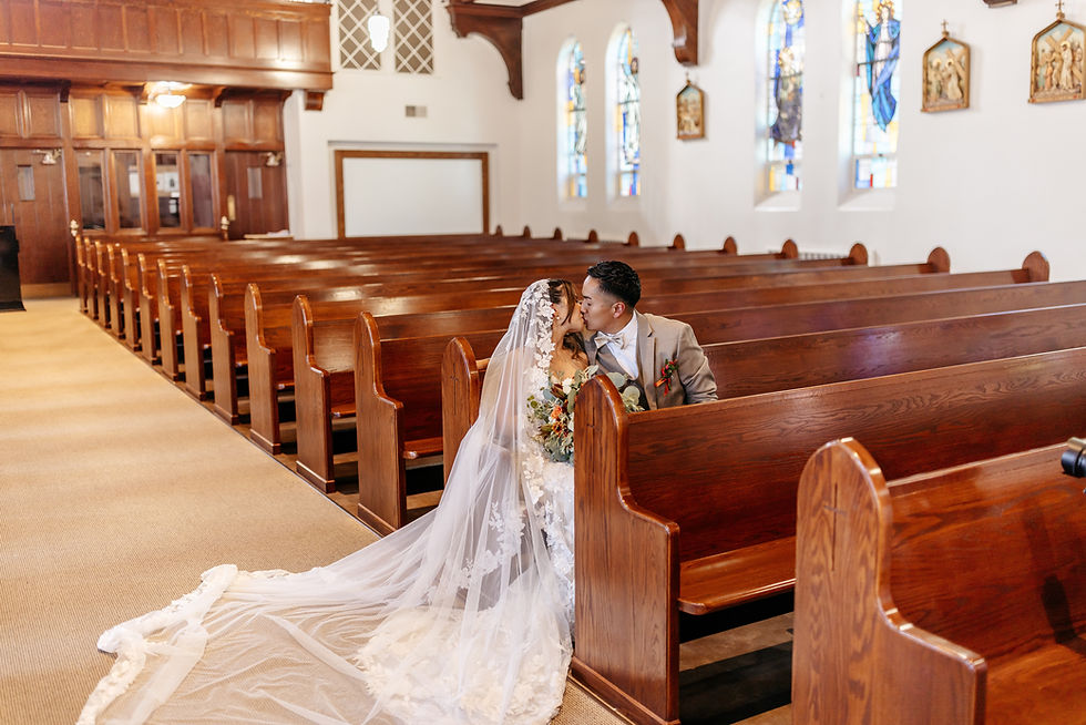 A bride and groom sitting and kissing in a catholic chapel.
