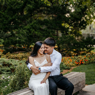 Gorgeous couple that is engaged in a garden. They are snuggled together. The woman is wearing a bride dress.