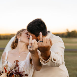 Bride and groom showing on their wedding rings while kissing. 