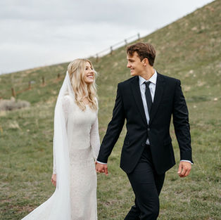 Bride and groom walking at the Tunnel Springs park. A green hill is in the background. Bride and groom and smiling at each other.