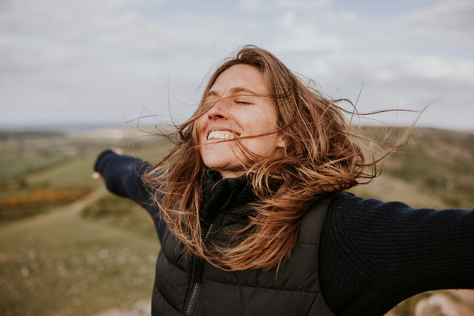 A happy blond woman with brown hair, arms outstretched, enjoying the nature outdoors. The