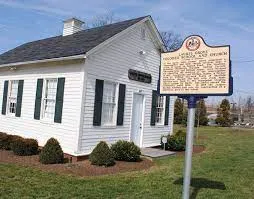 The historic marker for Laurel Grove Colored School and Church is shown with the one-room schoolhouse in the background.
