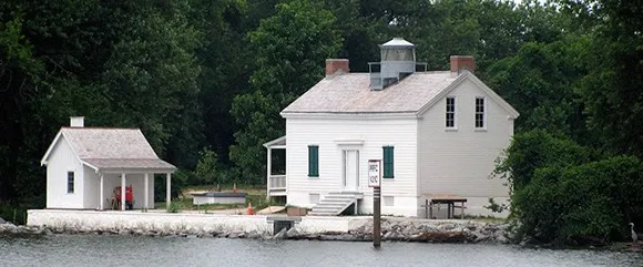 The Jones Point Lighthouse is photographed from the Potomac River with the trees of Jones Point Park in the background.