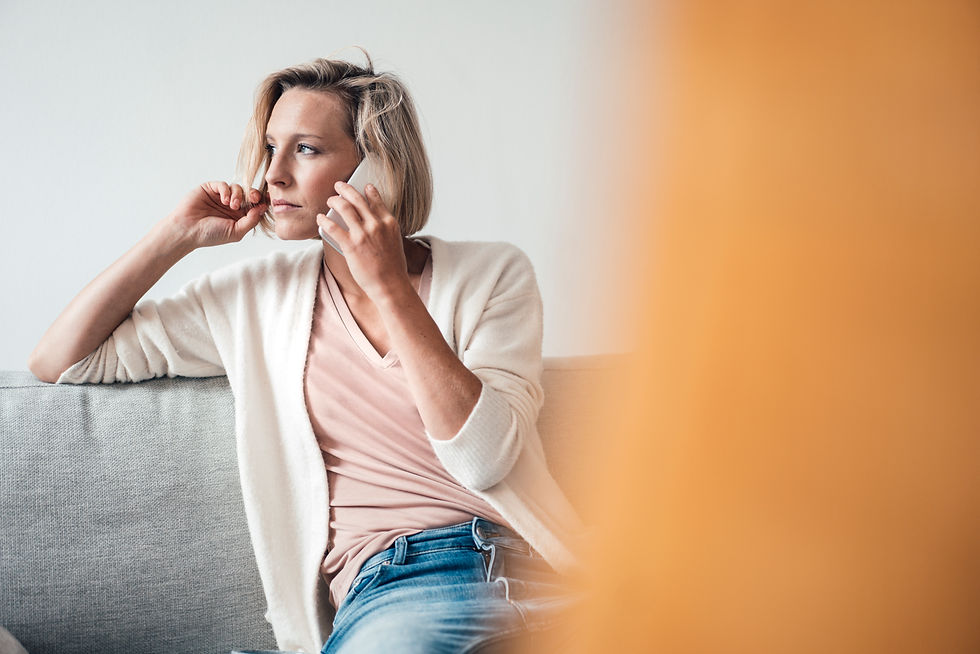 Jonge vrouw zit neer in sofa en telefoneert.