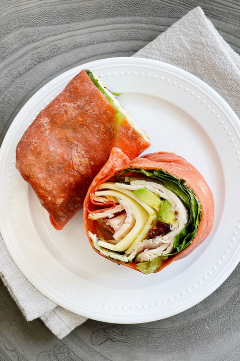 a turkey wrap made with a tomato tortilla cut in half on a plate.