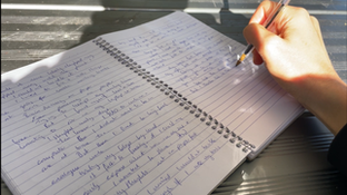 Image of a hand writing by hand in a notebook.