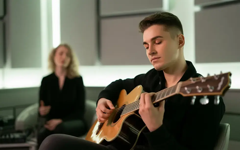 Vignette photo-réaliste 16:9 illustrant “Hypnose pour musiciens : comment ça fonctionne” : musicien adulte yeux fermés en légère transe avec guitare dans un studio moderne, hypnothérapeute flou en arrière‑plan guidant la séance.
