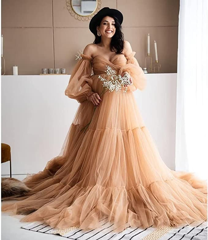 A woman in a black hat and champagne tulle maternity dress holding baby's breath and smiling.