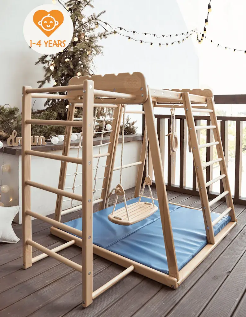 A play gym with wooden rings, rope climbing, a swing, and ladders in a kids play room.
