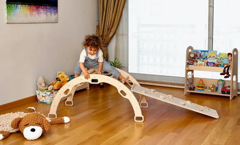 A toddler climbing on a wooden arch in his playroom.