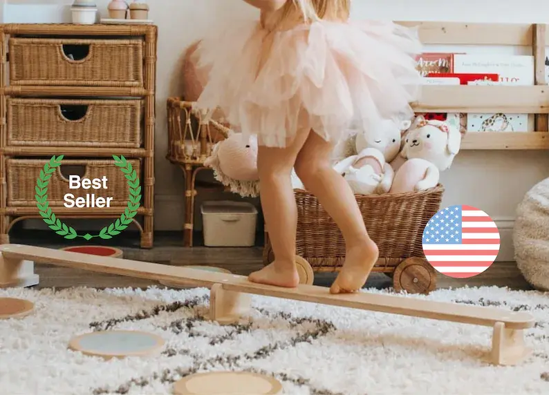 A toddler in a pink tutu walking across a wooden balance beam in the play room.
