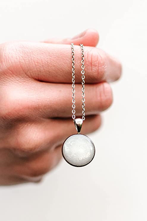 A woman holding a simple circle necklace made of breastmilk.