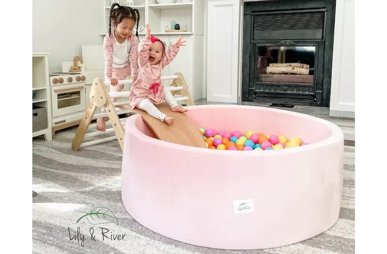 Two young girls sliding into a large, pink ball pit.