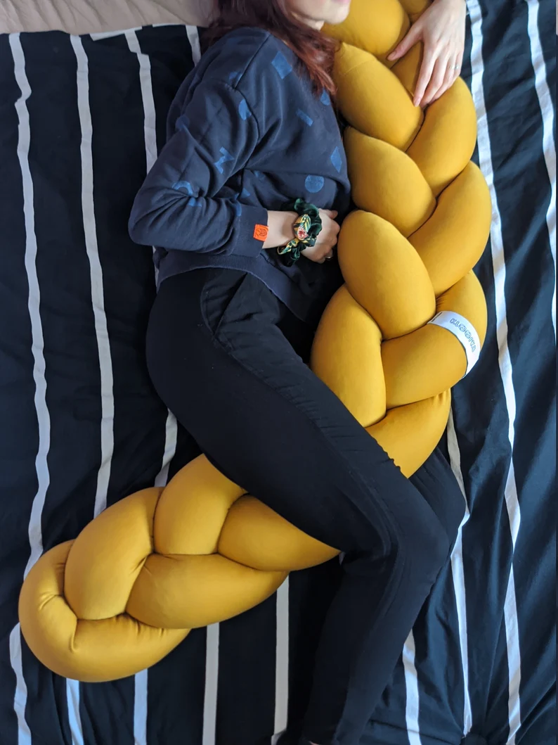 A brunette woman laying on a blue bed hugging a braided body pillow.