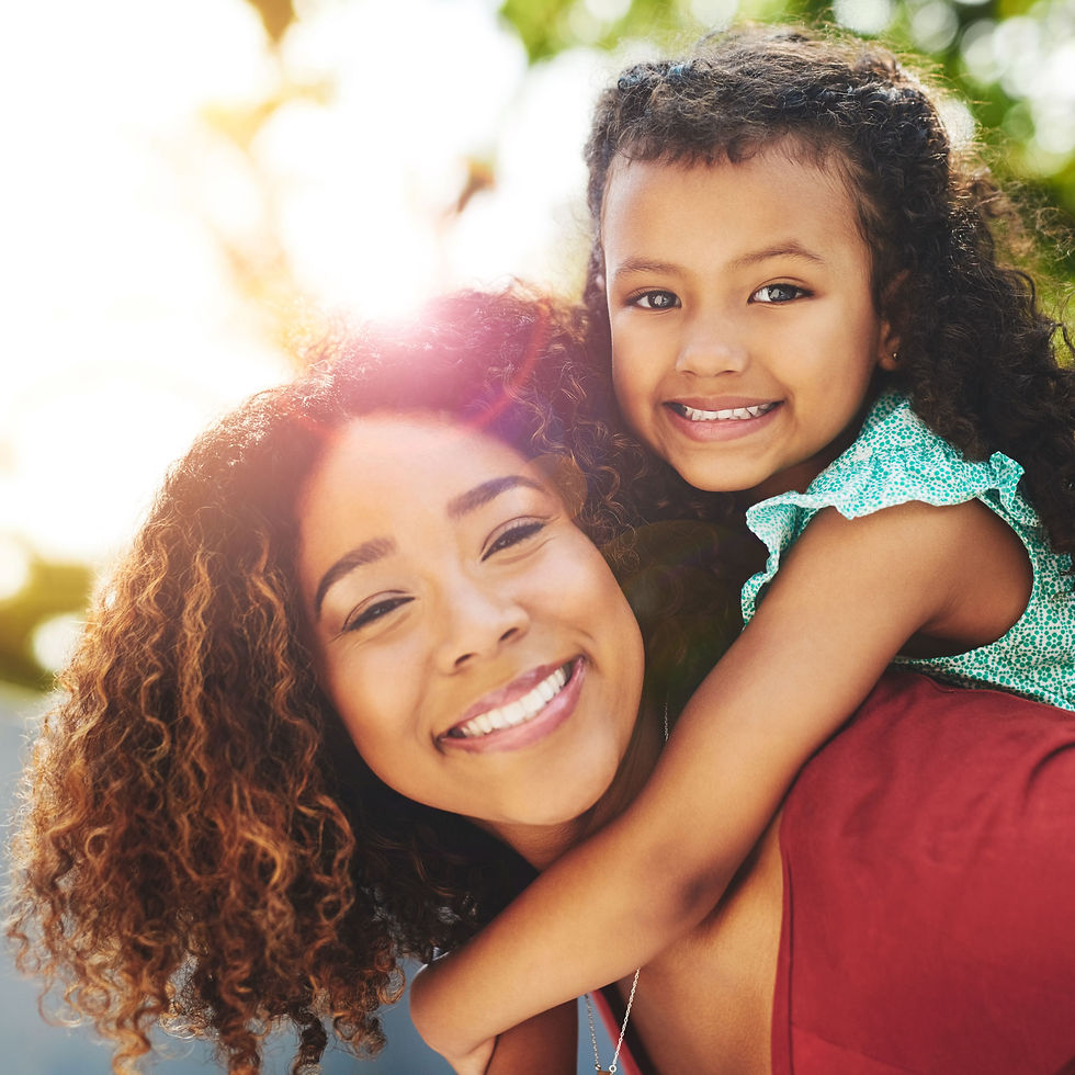 A woman with her toddler daughter on her back both smiling with the sun behind them.