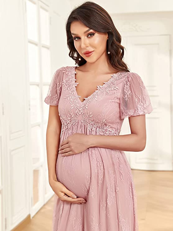 A woman holding her baby bump and smiling in a lacy pink maternity gown.