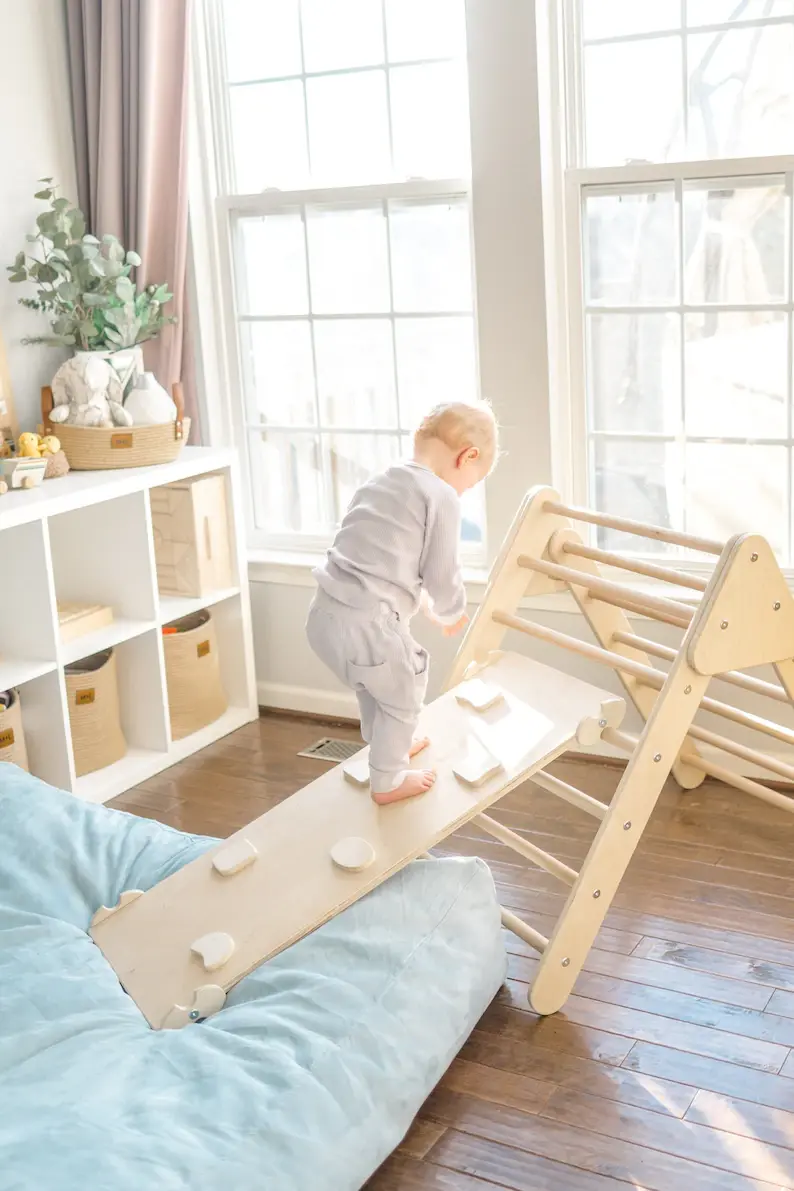A toddler boy climbing up a wooden rock wall play gym in his living room.