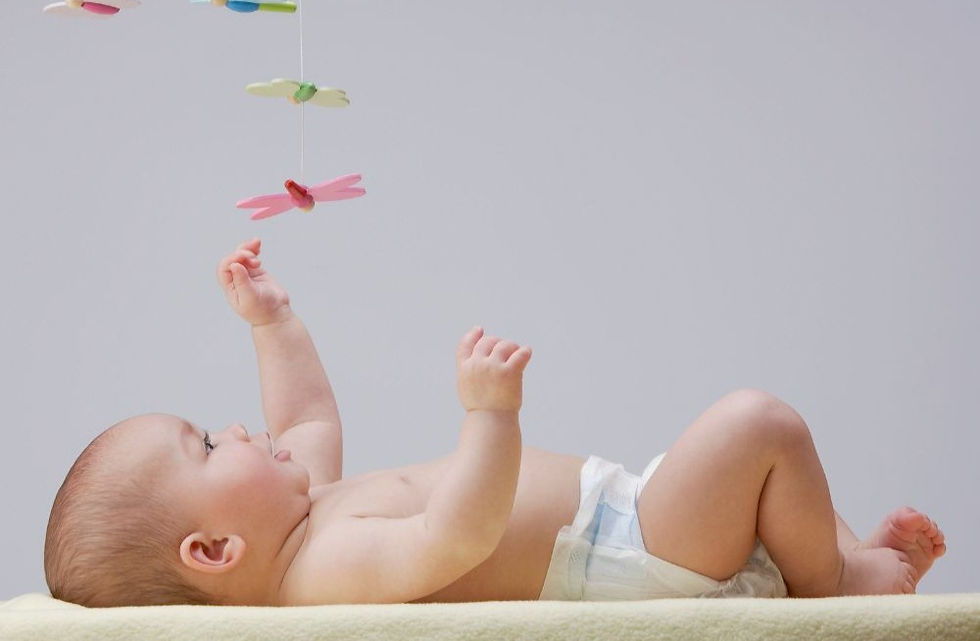 A newborn baby playing with a colorful toy on his back.
