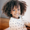 A smiling toddler girl with curly hair and a white polka dot shirt.