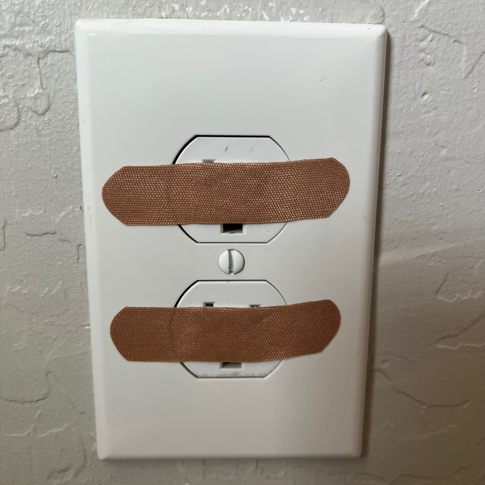 Two bandaids covering up the outlet holes on a wall outlet.