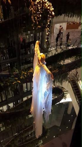 In een betoverende witte jurk zweeft een vrouwelijke luchtacrobaat boven het publiek, haar gracieuze pose in de lucht vormt een symbool van hemelse schoonheid en artistieke perfectie