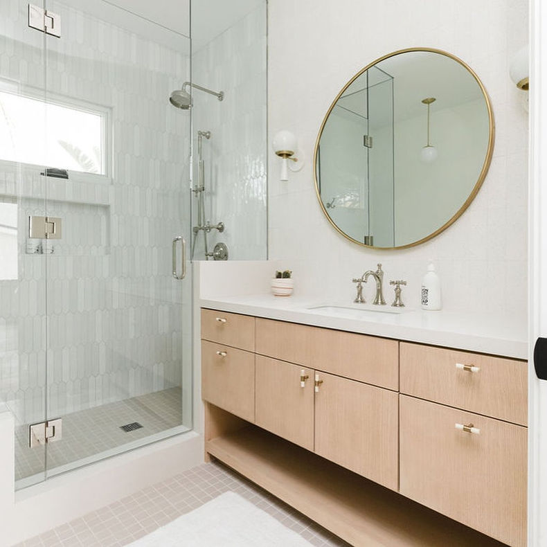 Small bathroom remodeling idea by Kitchen and Bath Beyond in San Diego | Small walk in shower with hinged single glass door, tiled shower walls, drop in sink with circular mirror, wooden drawers, and granite countertop