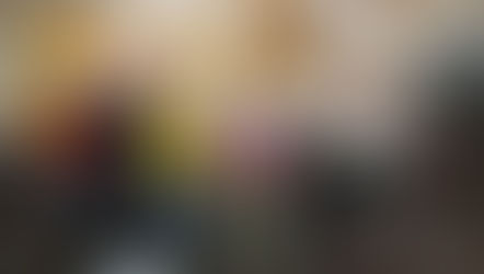 A diverse choir practices in a warmly lit room with wooden beams and flags. Members hold music sheets, focusing intently on singing.