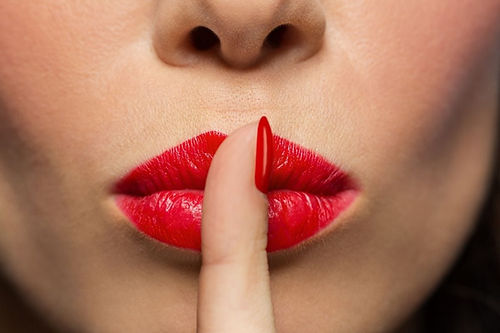 quiet-silent-appointment. photo. lower half of a womans face wearing bright red lipstick with her index finger over her lips giving the "Shhh" sign