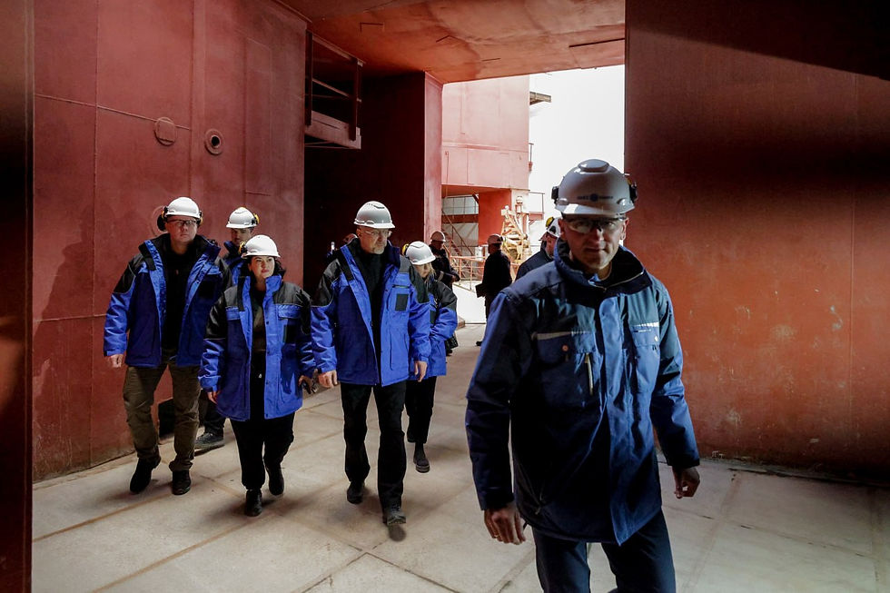 A group in hard hats and blue jackets walking through a red-walled industrial hall at a Ukrainian nuclear power plant