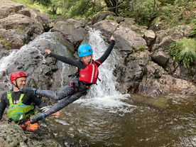 Kid jumping out into a pool in a Ghyll watched by an instructor.