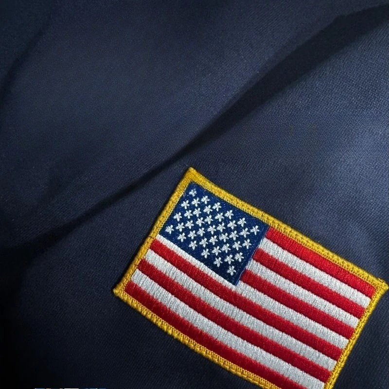 Thumbnail: Close-up of American flag embroidery on a navy pullover.