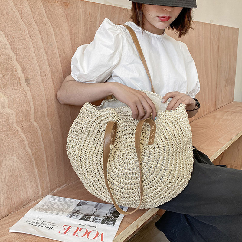 Thumbnail: Woman holding a round handmade woven straw shoulder bag.
