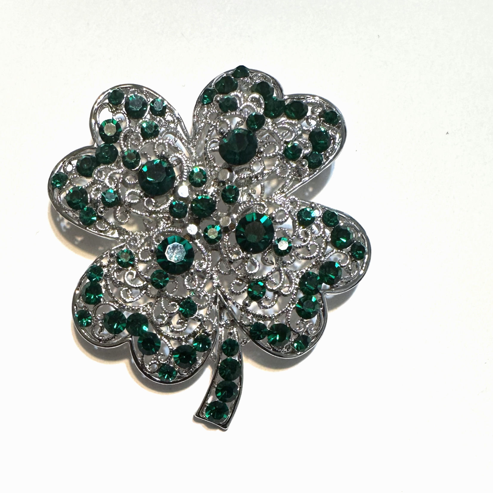 Sparkling four-leaf clover brooch with green gems on white background.