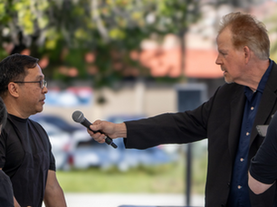 man in a suit jacket holding out a microphone to interview another man