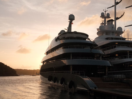 Luxury yacht at sunset in calm bay, with dark silhouette, glowing sky, and distant shoreline.