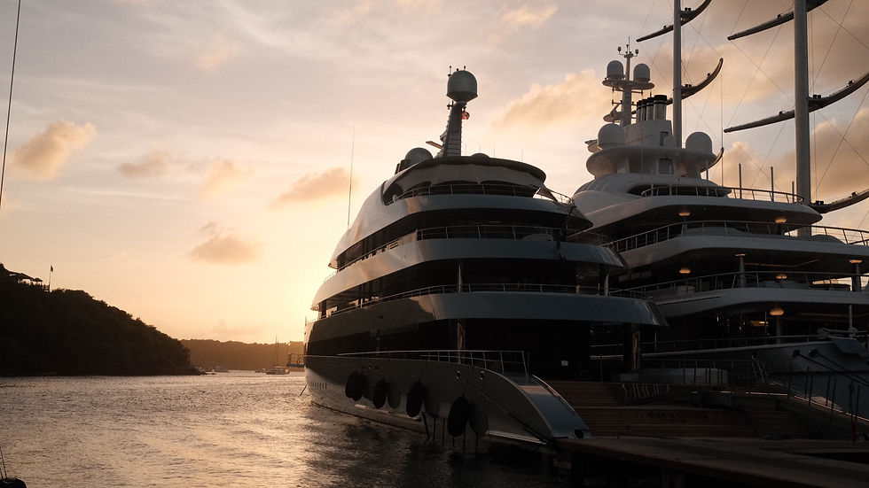 Luxury yacht at sunset in calm bay, with dark silhouette, glowing sky, and distant shoreline.