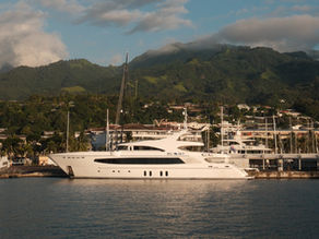 White yacht BIG SKY at a tropical marina with sailboats, green mountains, and clouds in warm evening light.