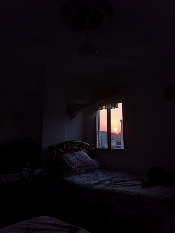 A bedroom window with a warm sunset view beyond — the transition from day to evening.