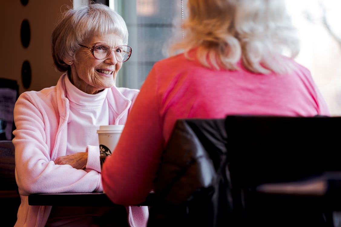 Two older women sharing coffee and genuine conversation — the warmth of a real relationship over time.