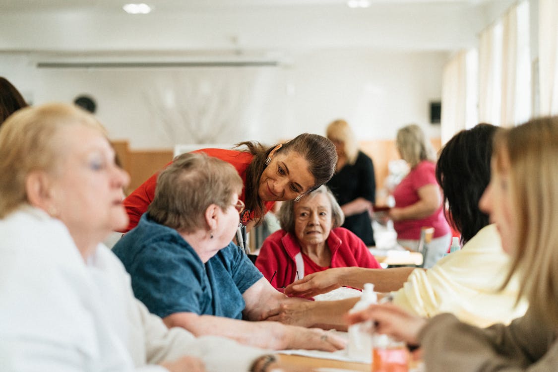 A caregiver engaging warmly with a group of seniors at a table — genuine connection, not a rotation.