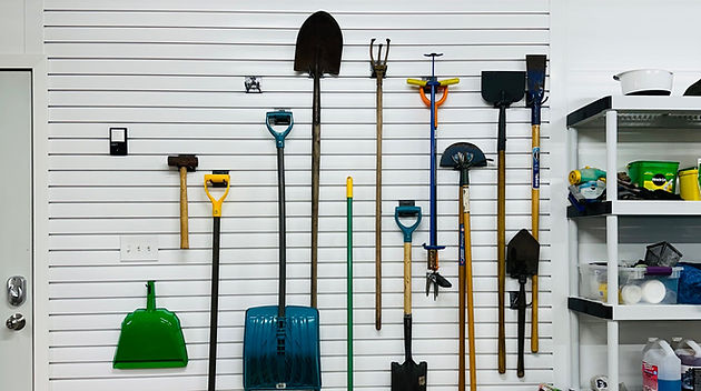 Wall of neatly arranged gardening tools and snow shovels stored in an organized space.