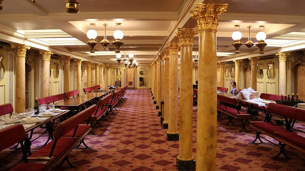 Ornate ship dining room with gold columns and red benches; one woman stands near a table set with dishes and bottles.
