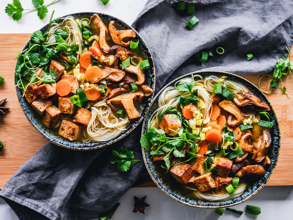 Two bowls of food including noodles, mushrooms, carrots, and tofu. They are topped with spring onion and coriander